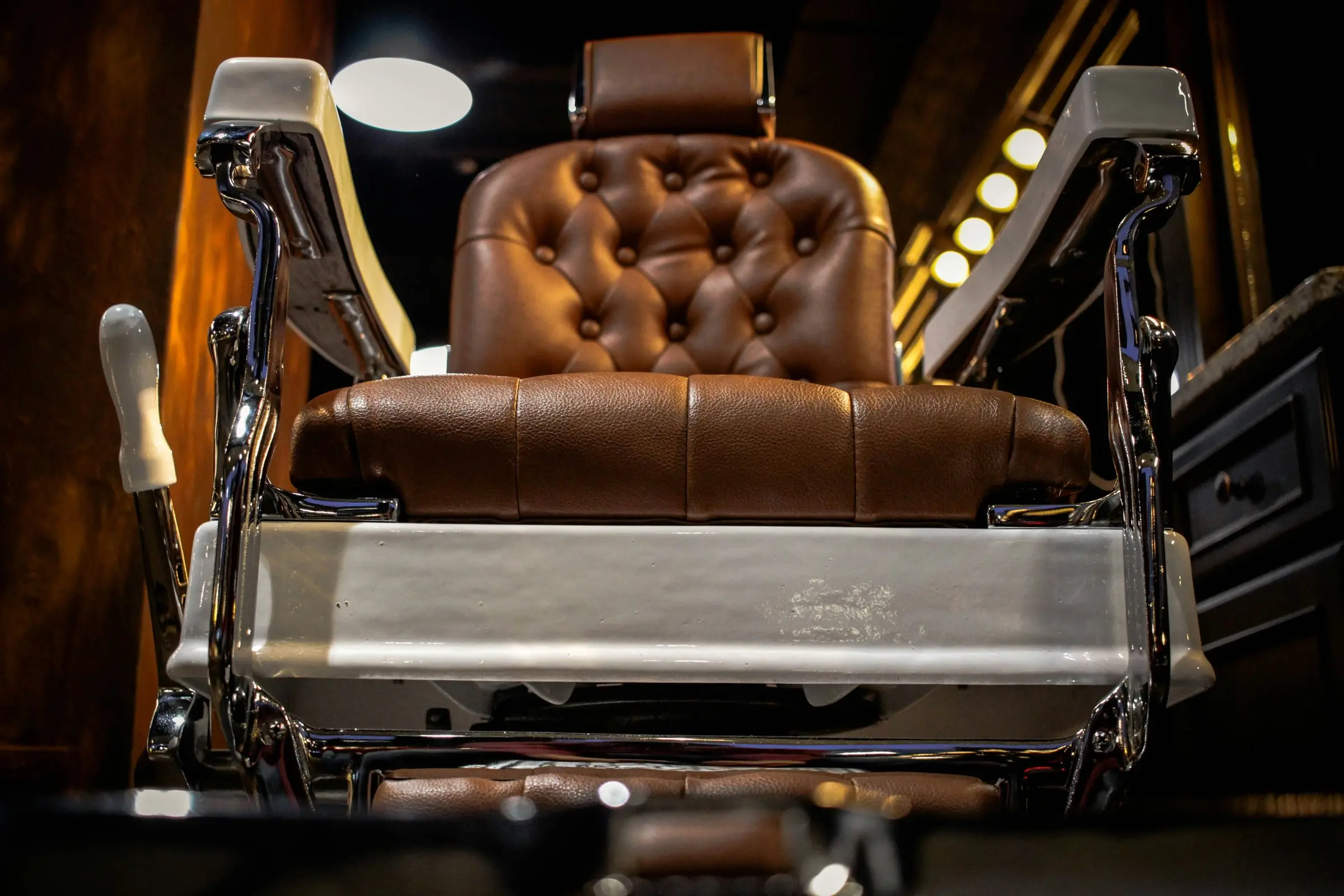 Vintage barber chair: tufted brown leather, chrome frame, porcelain footrest, warm shop light