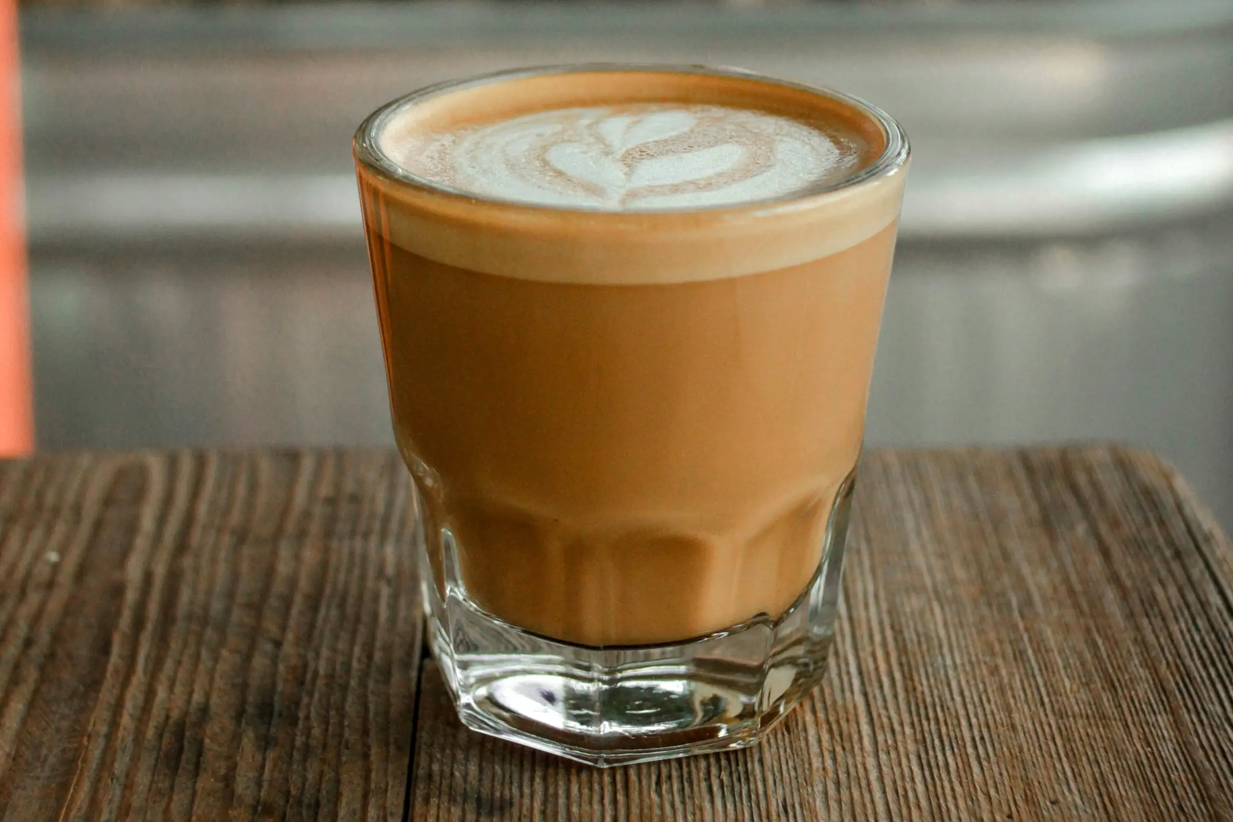Cortado with latte art in a Gibraltar glass on a weathered wood counter