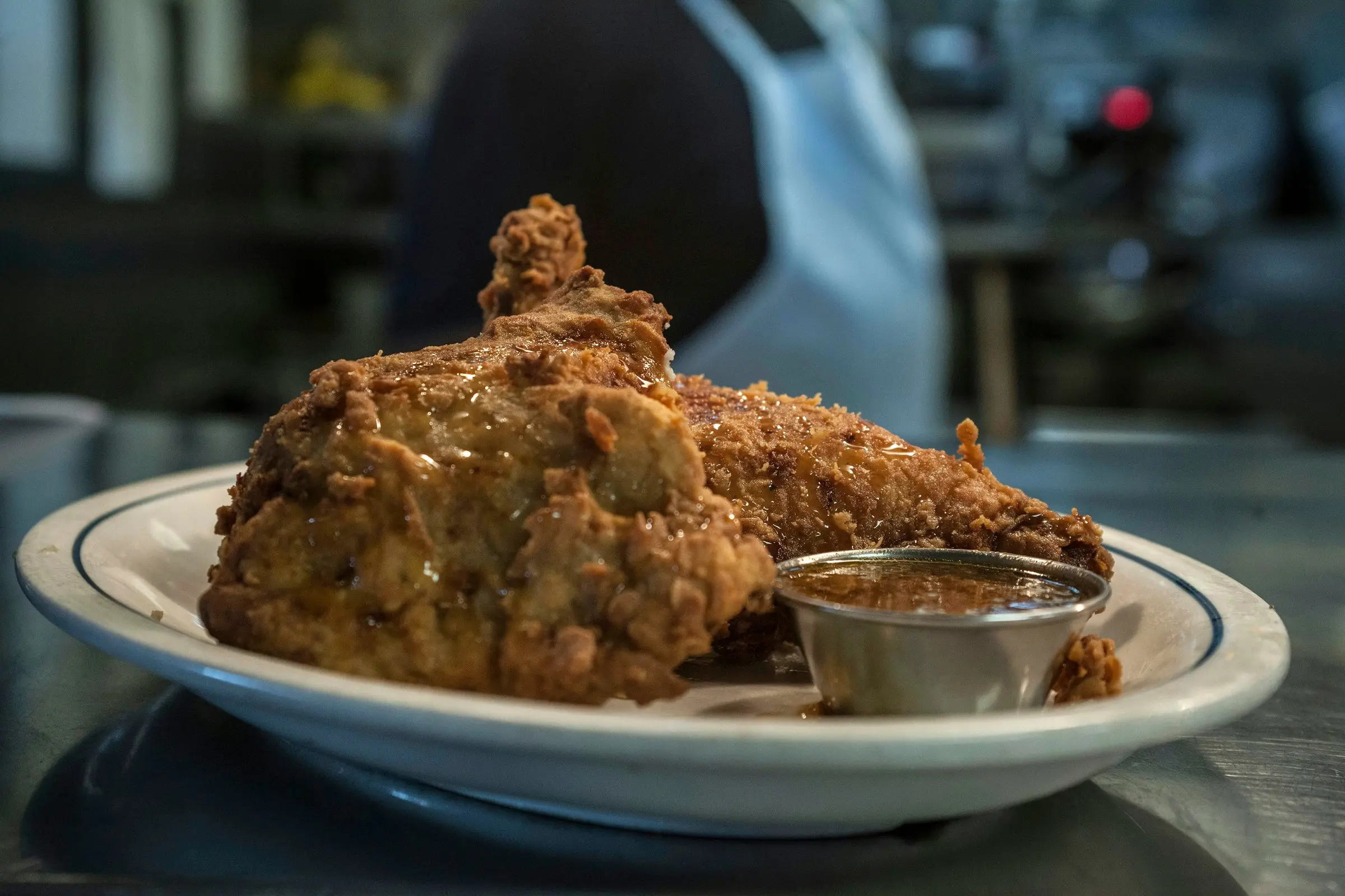 Southern fried chicken on a blue-rim diner plate with gravy, 45-degree view, cook blurred behind