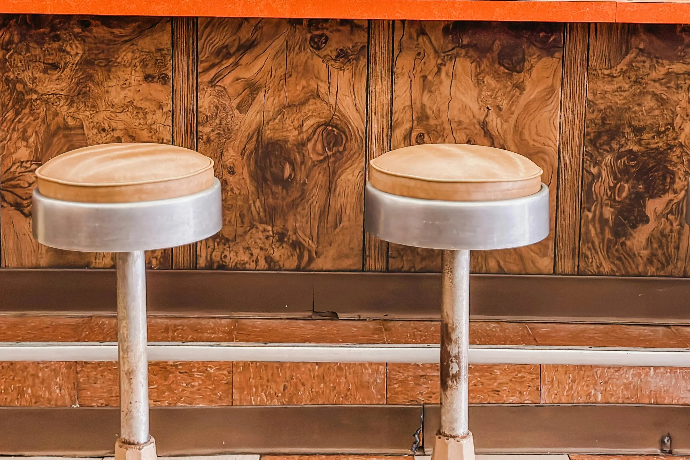 Lunch counter: worn aluminum stools with tan vinyl seats, burl wood-grain counter front, orange countertop