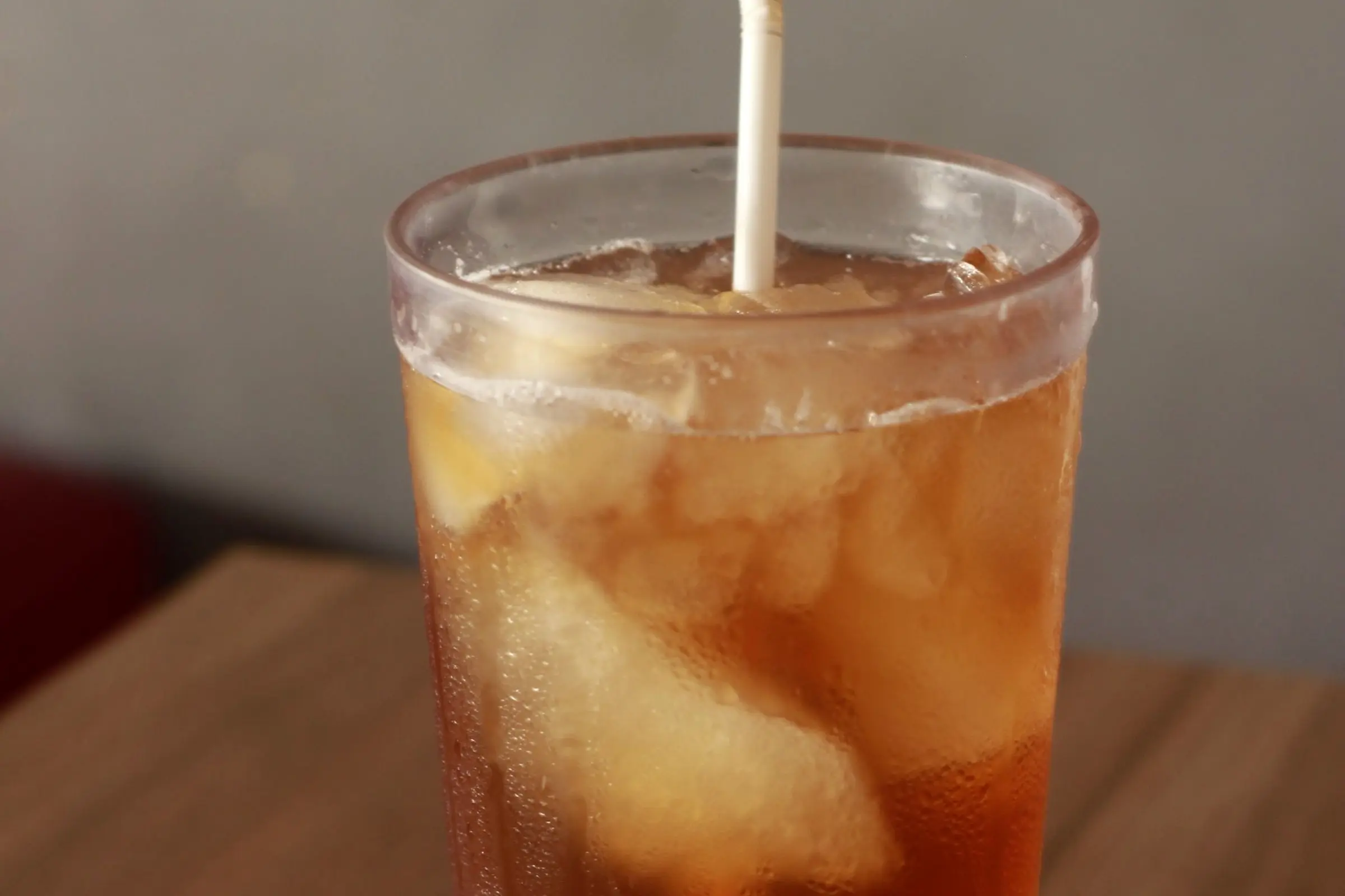 Iced tea with a lemon wedge in a pebbled plastic restaurant tumbler on a wood table